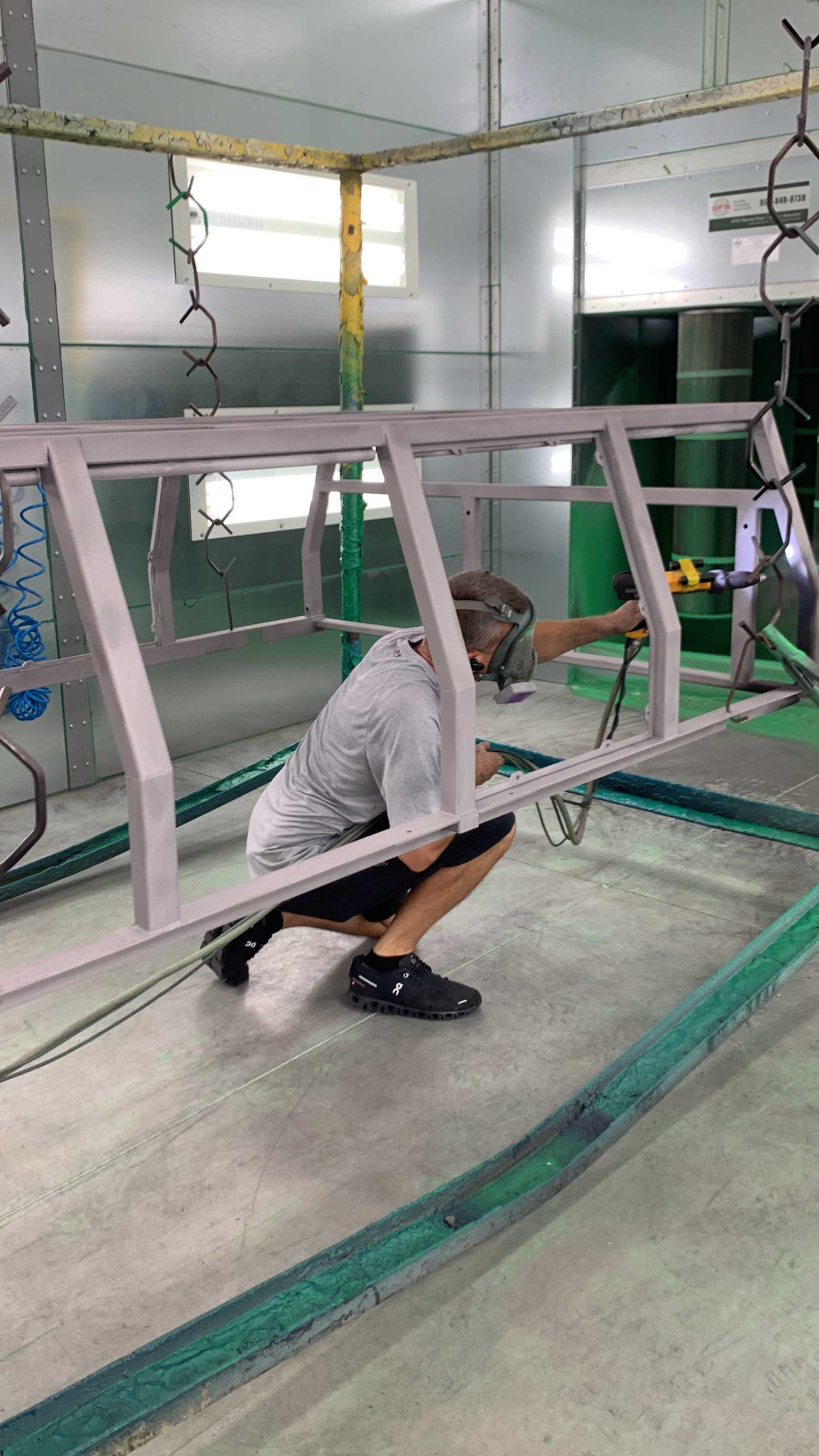 A man applies a gray-colored coating to a metal frame.