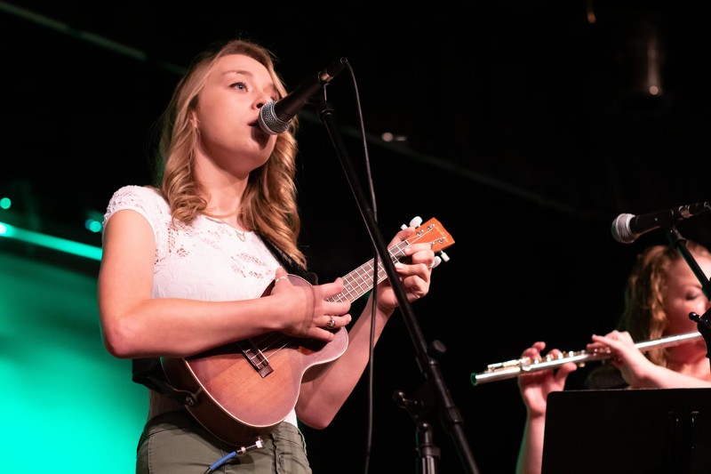 A young girl plays a small guitar while on stage.