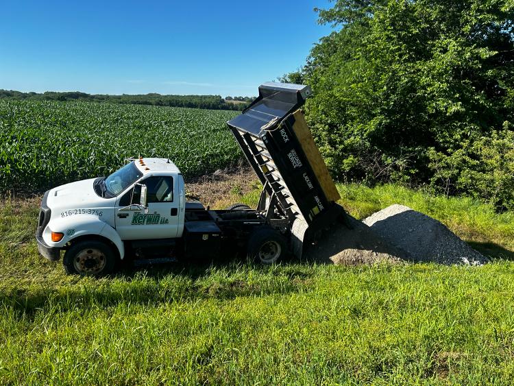 A dump truck unloads a pile of gravel onto the ground.