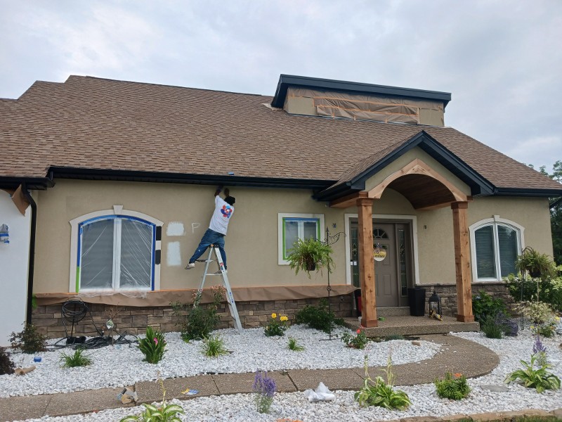 A man stands on a stepladder while painting a home’s exterior.