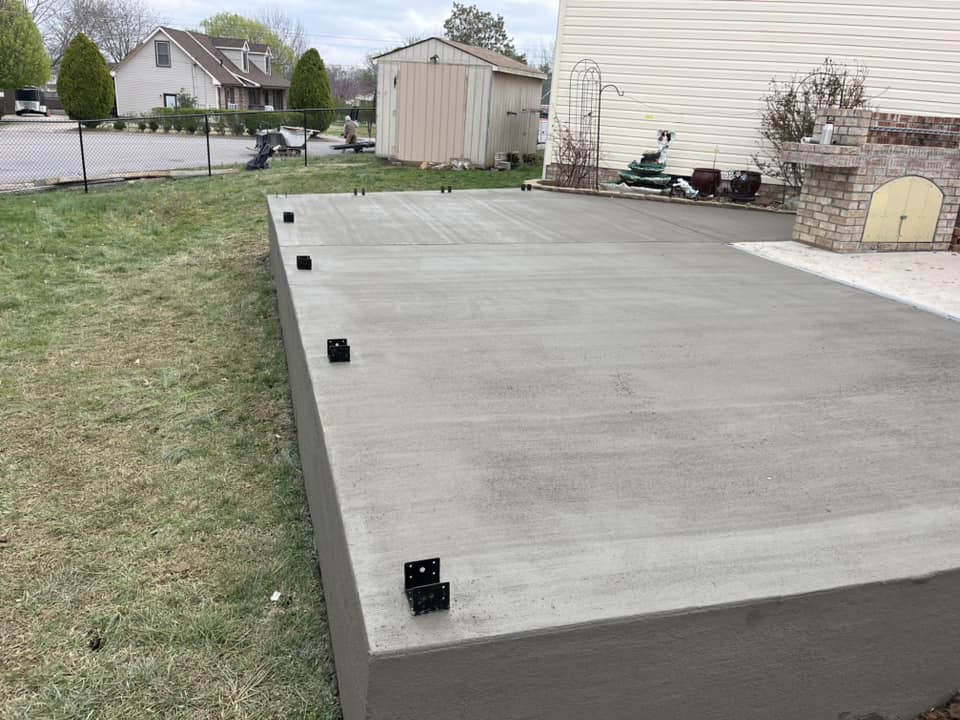 A freshly poured concrete pad next to a home and patio.