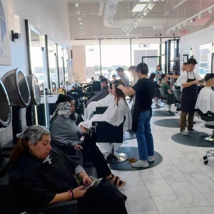 Rows of chairs at a salon are filled with customers receiving cuts and hair treatments.