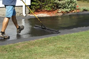 A man sprays sealcoating on an asphalt walkway.