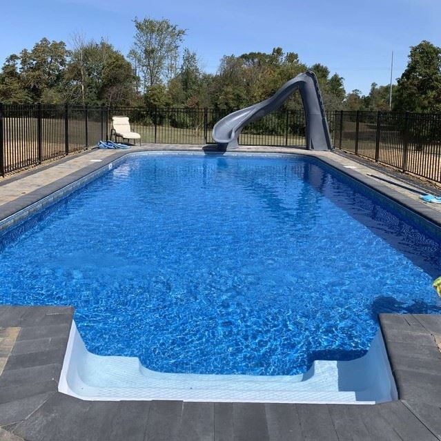 A fenced-in rectangular pool with a three-step walk-in entrance and a curved slide on the far end.