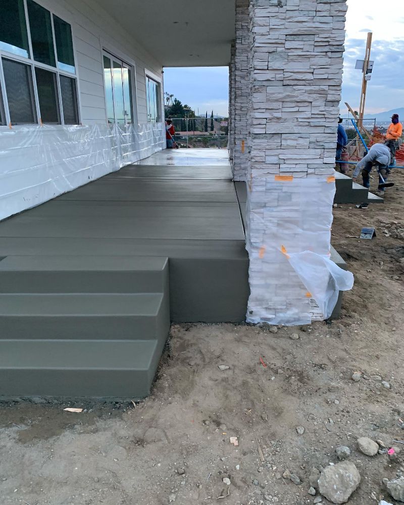 The side view of a new home with a freshly poured concrete patio with three levels of steps.