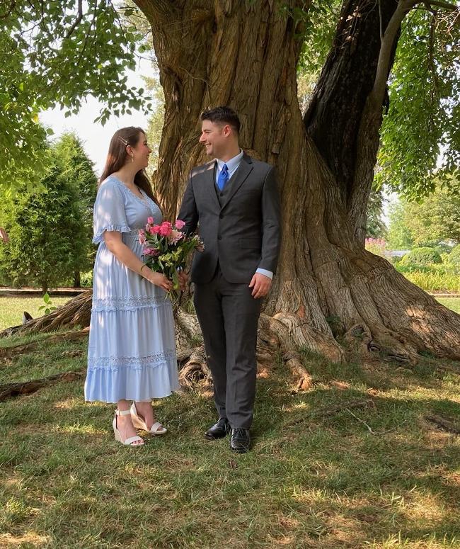 A bride and groom look at each other while standing underneath a large tree.