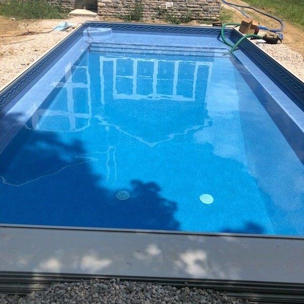 The reflection of a house shimmers in the water of a rectangular pool.
