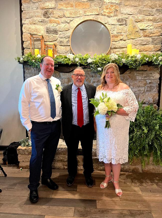 A bride and pose for a photo with a wedding officiant.