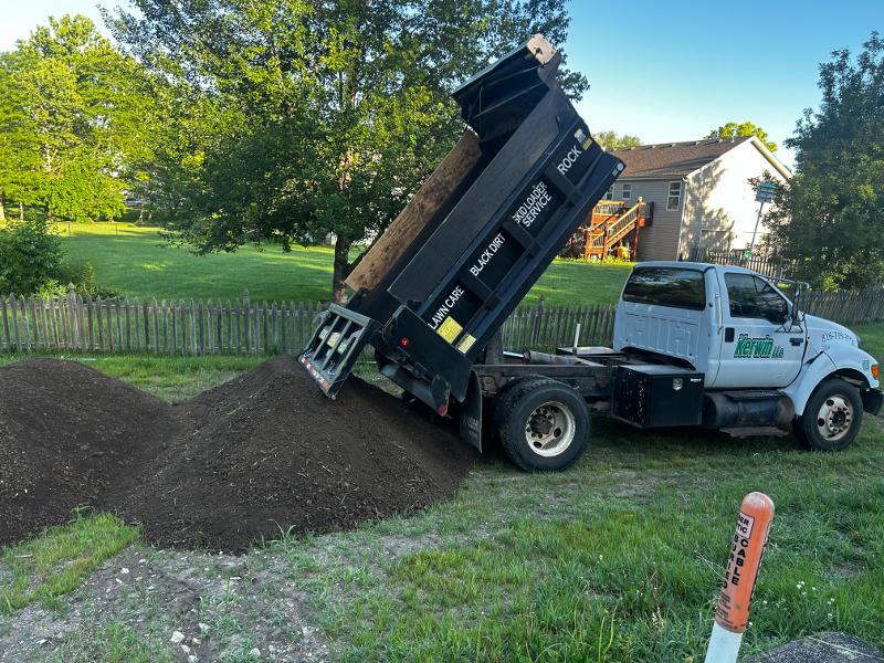 A dump truck unloads a pile of topsoil on the ground.