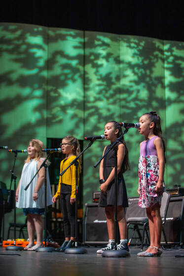 Four young children sing into microphones on stage.