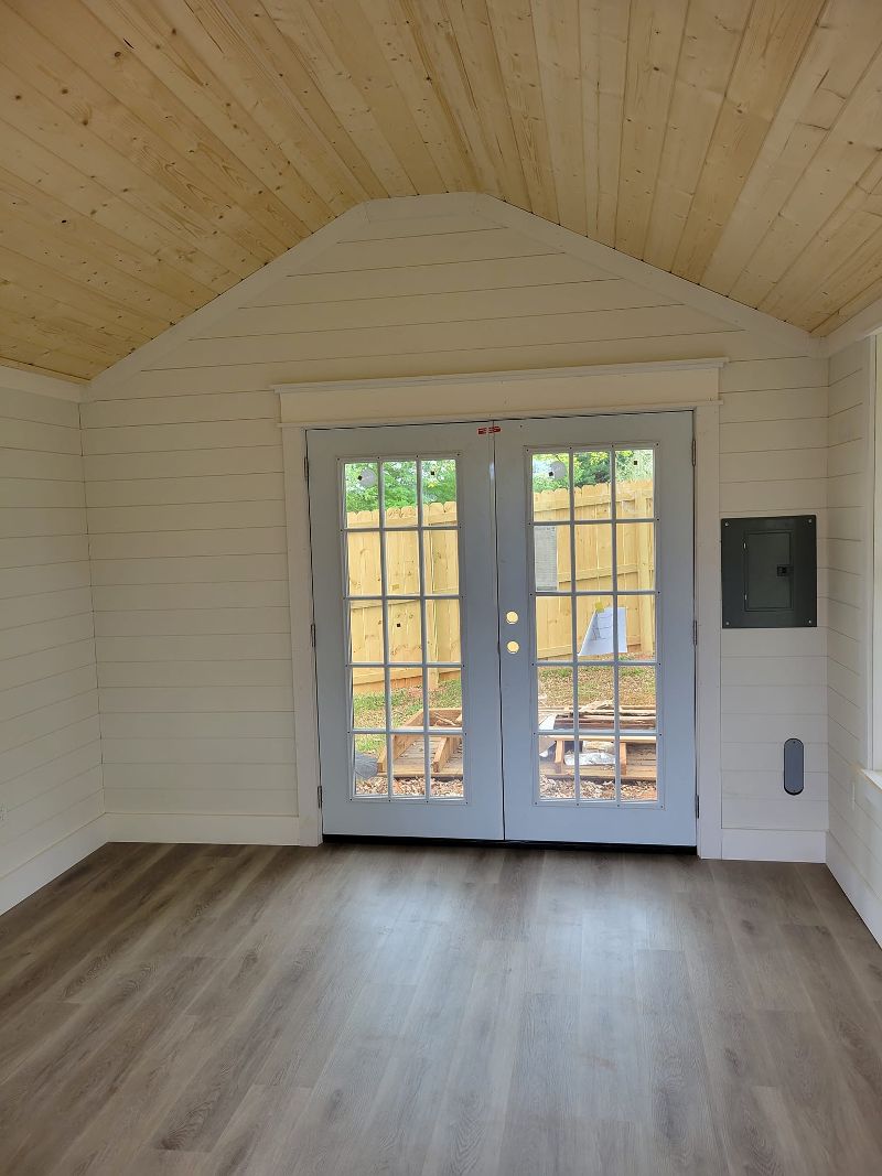 An open room with wood ceiling, wood walls, laminate flooring, and French doors leading outside.