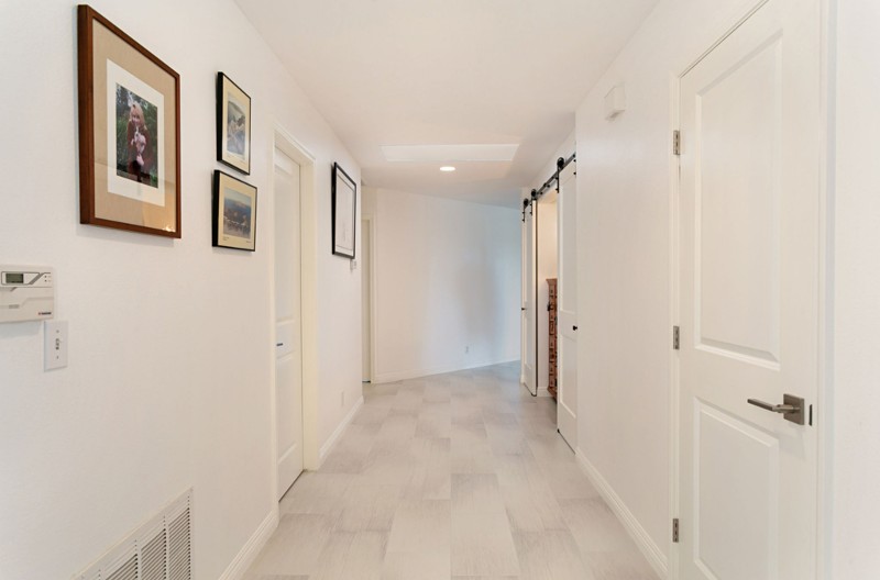 Remodeled hallway with white walls, white doors, and light wood floor