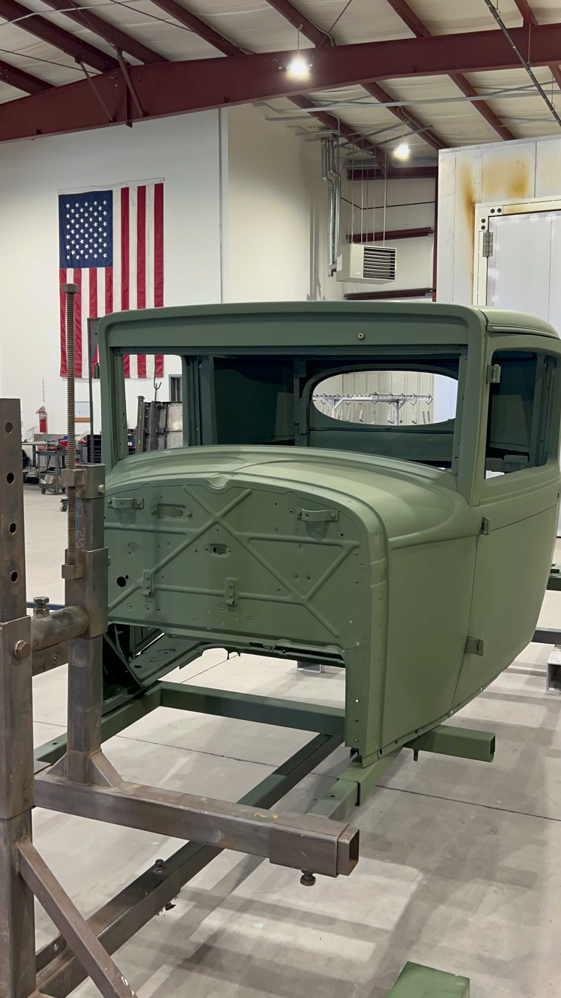 A classic truck body sits on a rack following light green powder coating.