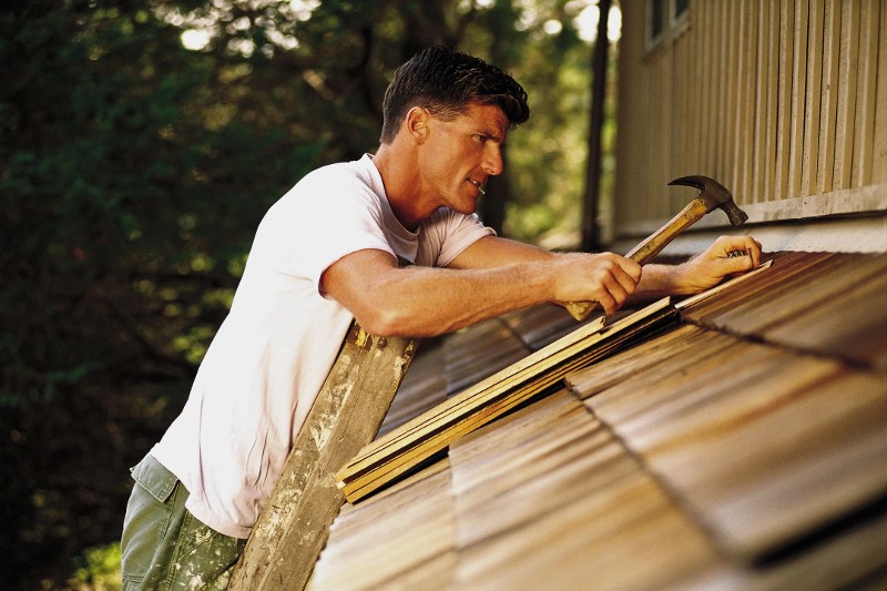 A roofer installs wooden shingles on a porch roof.