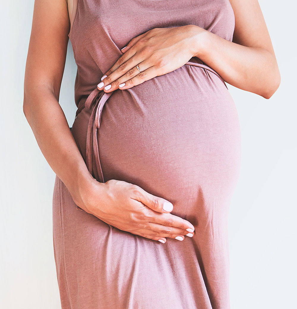 A pregnant woman wearing a flowing pink dress hold her belly gently