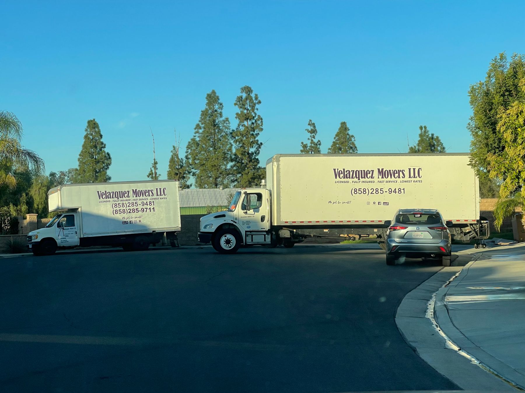 Two Velazquez Movers LLC moving trucks sit parked along the roadway.