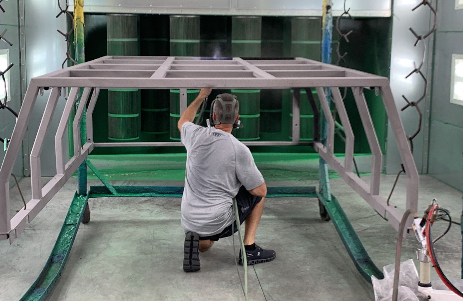 A man applies a gray-colored coating to a metal frame.