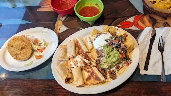 A large plate of burritos with nacho chips and guacamole and a side plate of salad and pork.