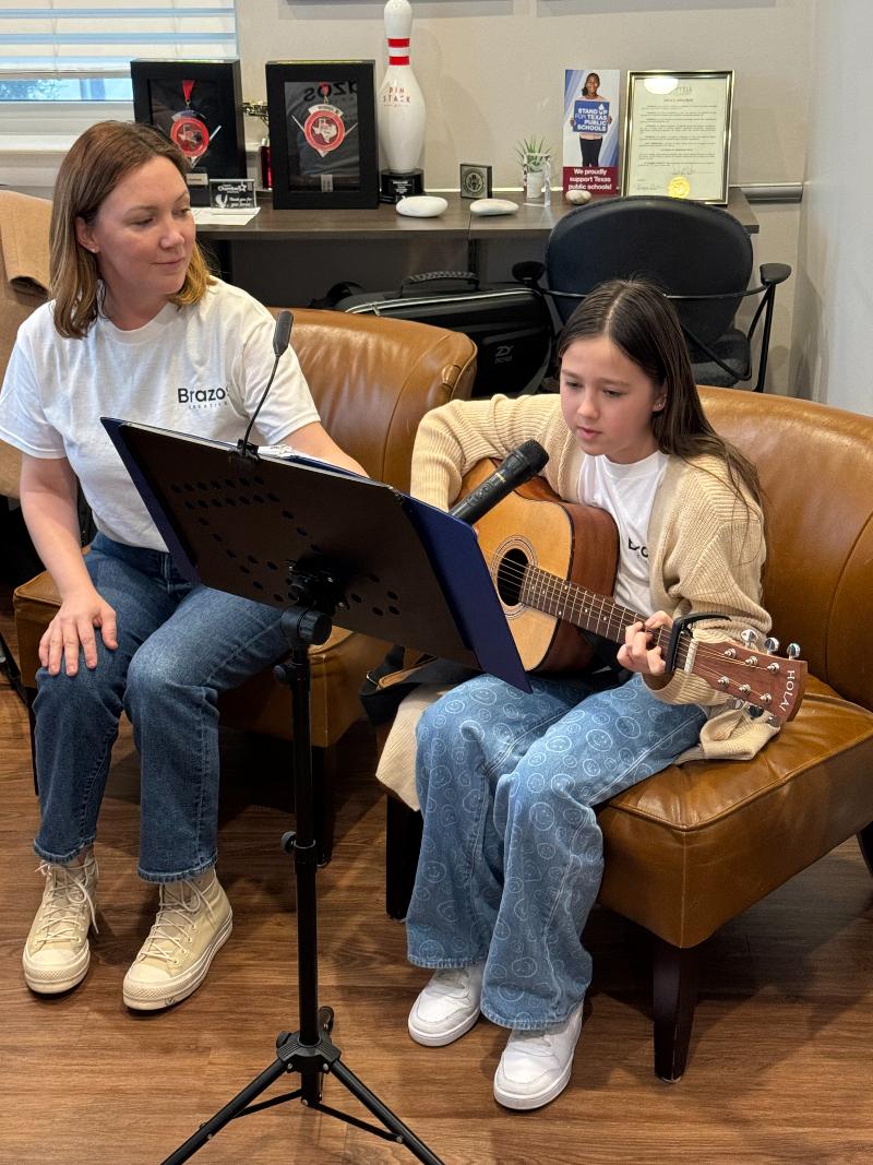 Instructor teaching a young girl to play guitar and sing.