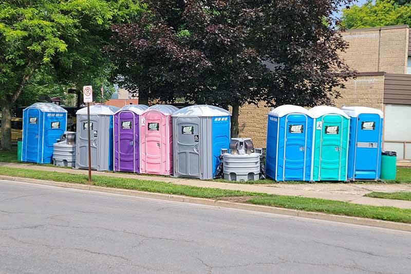 Eight portable toilets with two portable sinks situated in between them next to a roadway.