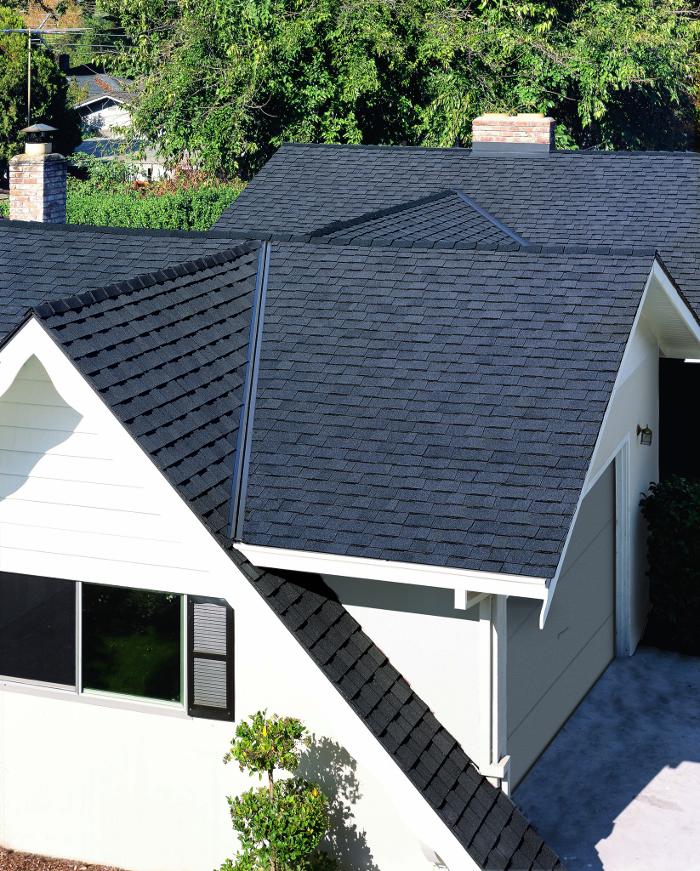 A white house with multiple gables of black shingles.