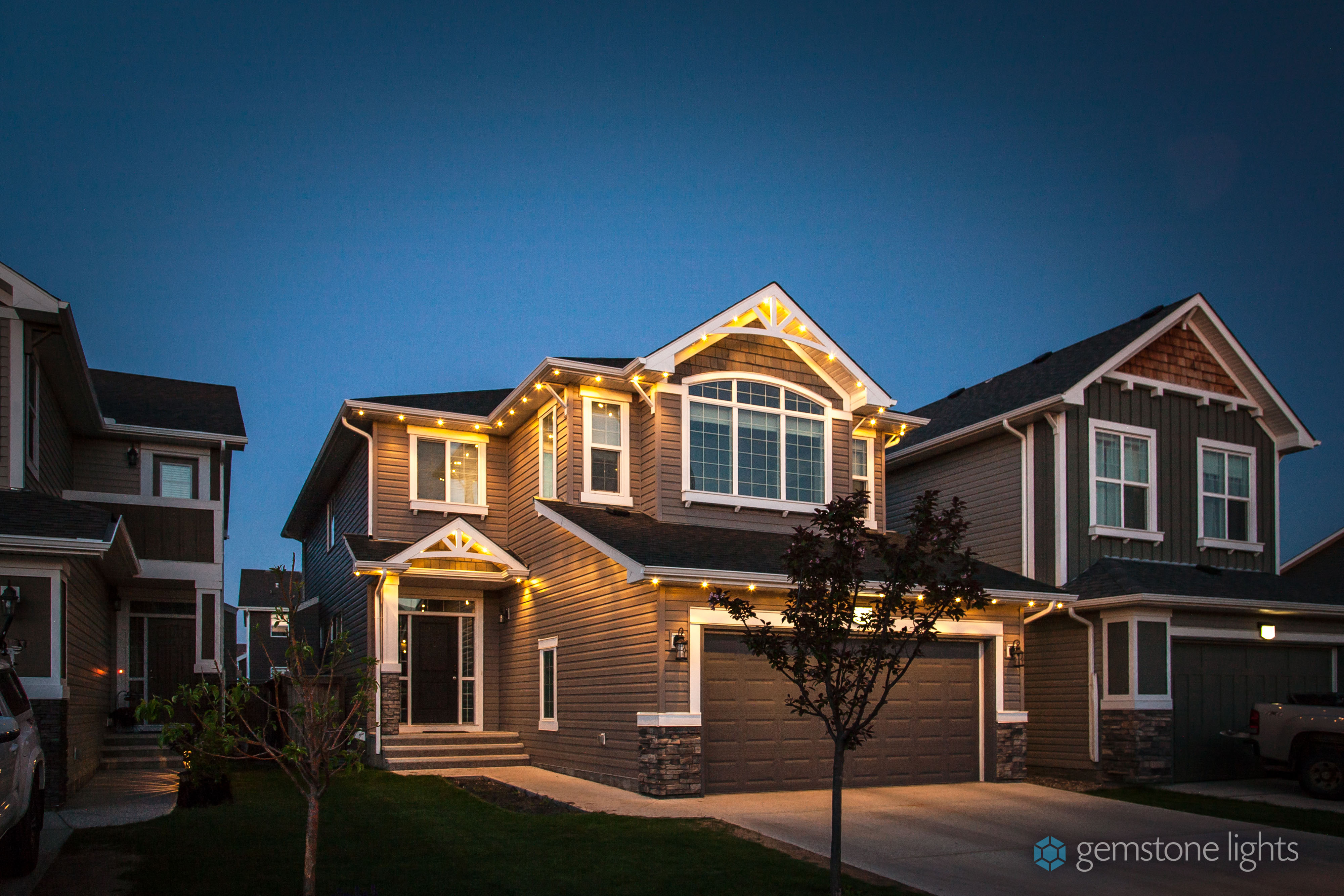 Gemstone Lights permanent architectural lighting illuminates the front of a gray house.