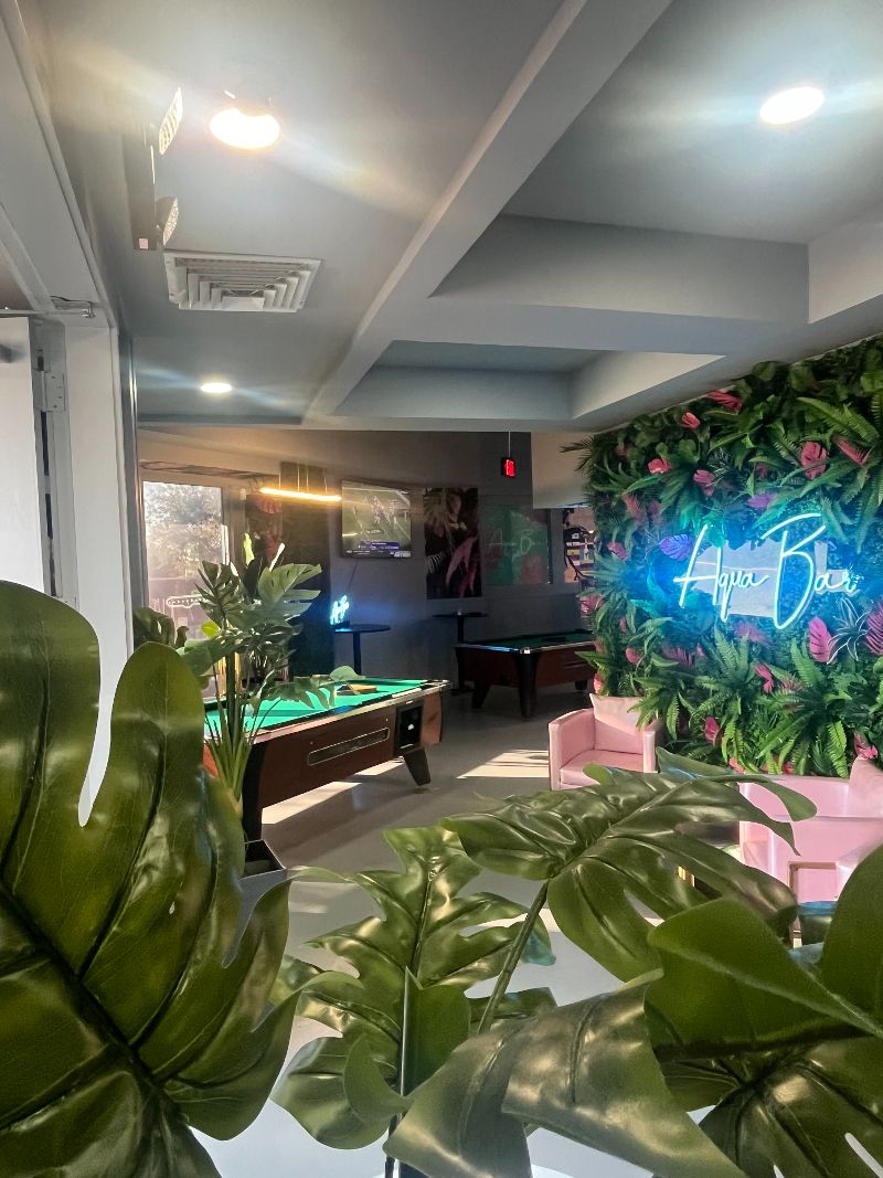 An inside scene inside Aqua Bar with a flowered wall and two pool tables.