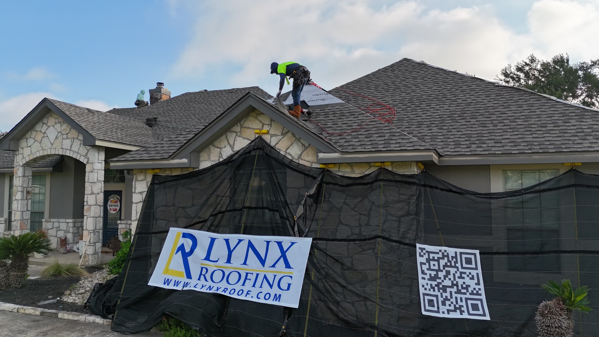 An advertising sign for Lynx Roofing leans against a tree.