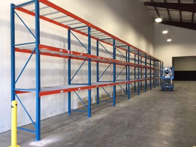 A three-level of shelving sits up against a warehouse wall.