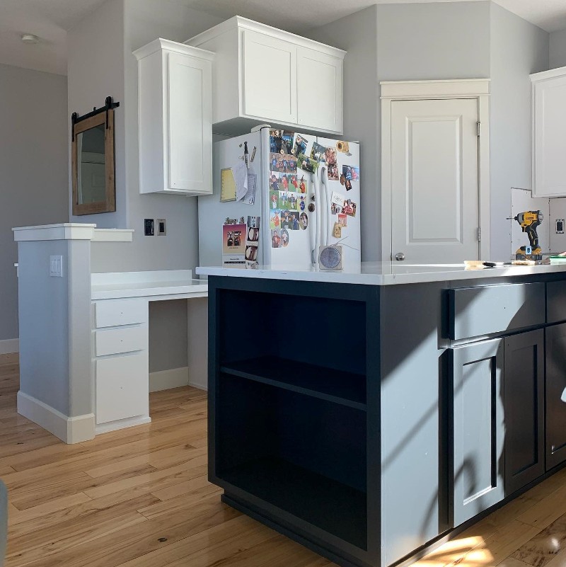 A kitchen with white cabinets and a dark grey island. 
