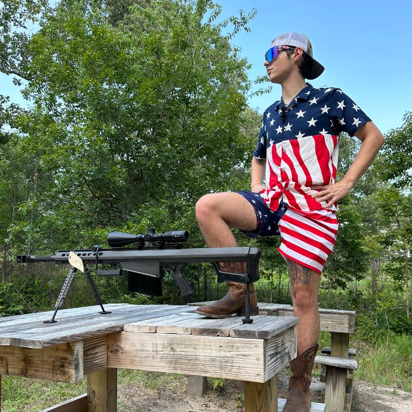 A man in patriotic clothing stands over a rifle mounted on a stand.