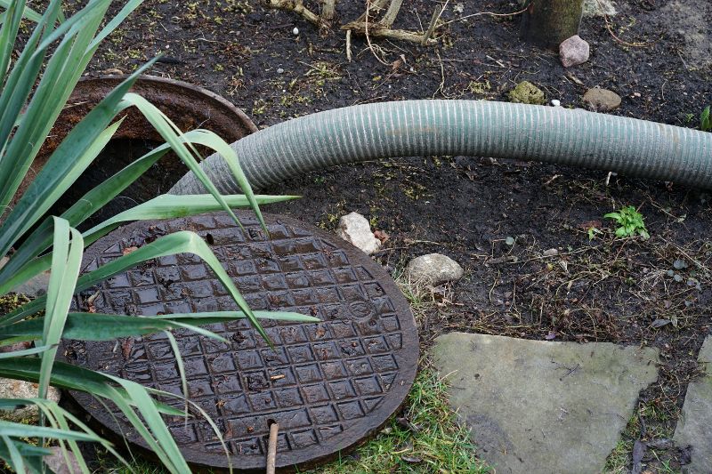 A hose is inserted into an outdoor septic tank.