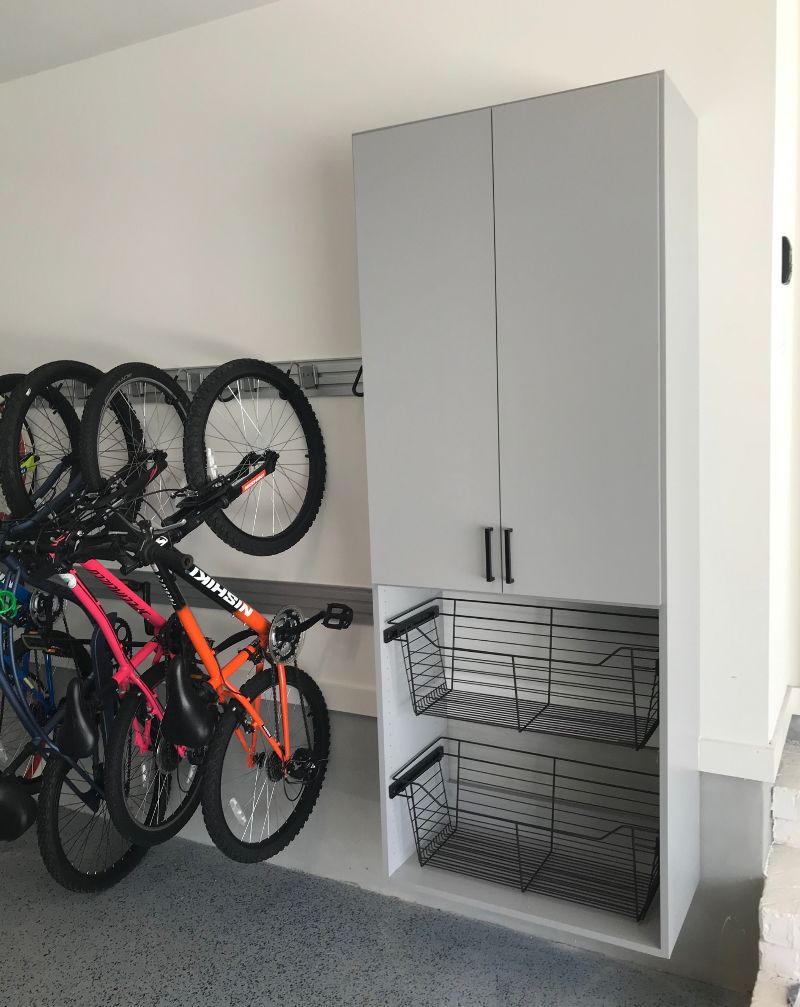 Three bicycles hang on a garage wall next to storage shelves with open bins on the bottom.