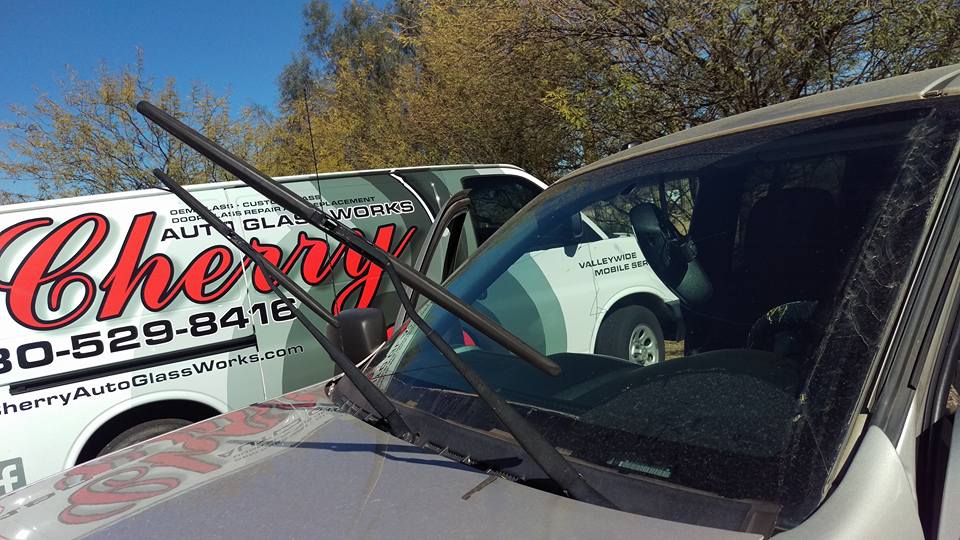 A Cherry Auto Glass Works van sits in a lot next to a gray car.